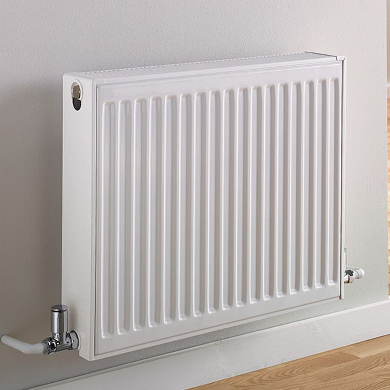 Compact white panel radiator with bottom pipe connections mounted on a light-coloured wall.
