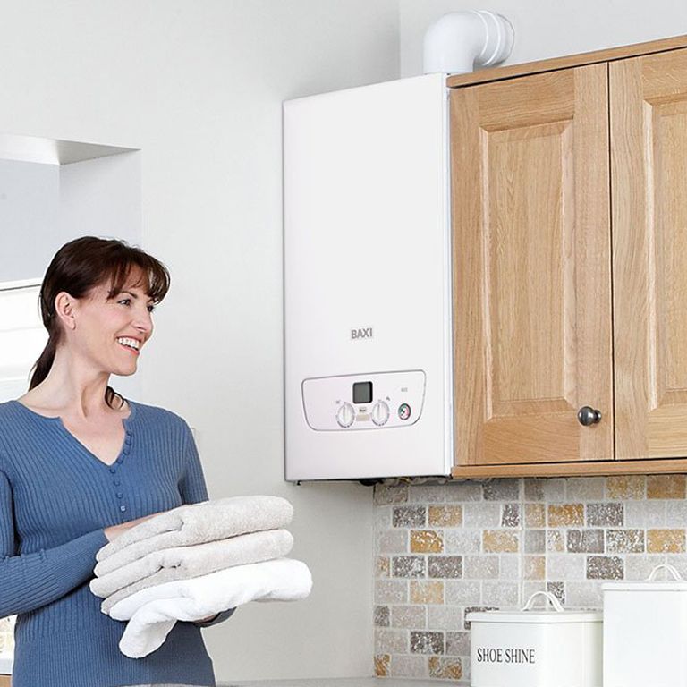 Modern white Baxi combi boiler installed in a kitchen cupboard with a smiling woman holding towels